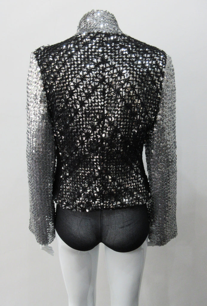 Silver Glitter Jacket with Black Crochet. Full on glittered siver colour sequin jacket with partblack crochet covered for a sporty feel. Crochet detailing unravelling/fraying in areas as done for intentional effect. CF zipper with 8.5cm high collar. CB length 52cm. Sleeve length from side neck point 76cm. 950g approximate weight. 90% Polyester, 5% Elastine, 5% Metallic Contrast: 100% Cotton. Lining: 100% Polyester. Dry Clean Only. Made in England