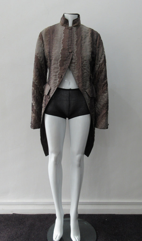 Brown Wave Cut Away Coat. Mid 19th Century military style cut-away coat in textured array of brown & brass. Slight reptile print covered with sheer stripe fabric pieces. CF cutaway and 29cm. CB slpit open back vent at hem. 2 button closure. CB length from neck point 91cm. Sleeve length from side neck point 80cm. 700g approximate weight. 75% Polyester, 25% Nylon Lining: 100% Rayon. Dry Clean Only. Made in Canada