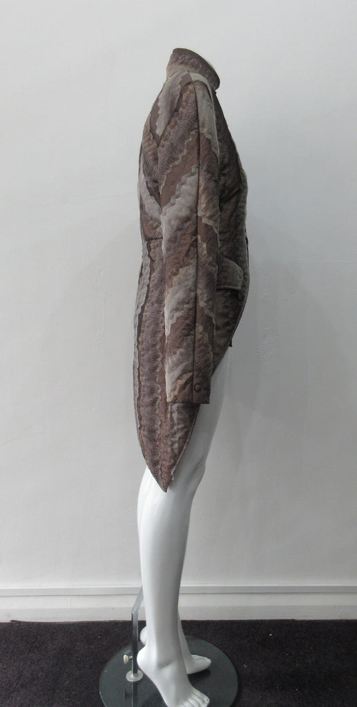 Brown Wave Cut Away Coat. Mid 19th Century military style cut-away coat in textured array of brown & brass. Slight reptile print covered with sheer stripe fabric pieces. CF cutaway and 29cm. CB slpit open back vent at hem. 2 button closure. CB length from neck point 91cm. Sleeve length from side neck point 80cm. 700g approximate weight. 75% Polyester, 25% Nylon Lining: 100% Rayon. Dry Clean Only. Made in Canada