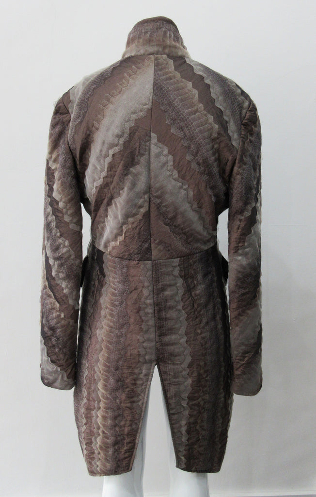 Brown Wave Cut Away Coat. Mid 19th Century military style cut-away coat in textured array of brown & brass. Slight reptile print covered with sheer stripe fabric pieces. CF cutaway and 29cm. CB slpit open back vent at hem. 2 button closure. CB length from neck point 91cm. Sleeve length from side neck point 80cm. 700g approximate weight. 75% Polyester, 25% Nylon Lining: 100% Rayon. Dry Clean Only. Made in Canada