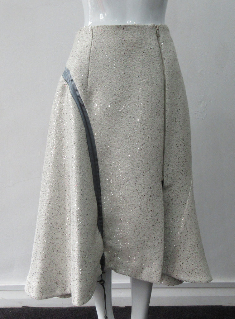 Plain Curve Panel Skirt Assymetrical gathered toggled skrit in grey-white colour. Grey seam panel can be gathered to create raised ruching effect. Featuring textured tweed style with spaced sequins. Large metal side front detaching zipper. CB length 80cm. 600g approximate weight. 36% Polyester, 28% Viscose, 35% Cotton, 5% Lycra. Dry Clean Only. Made in England