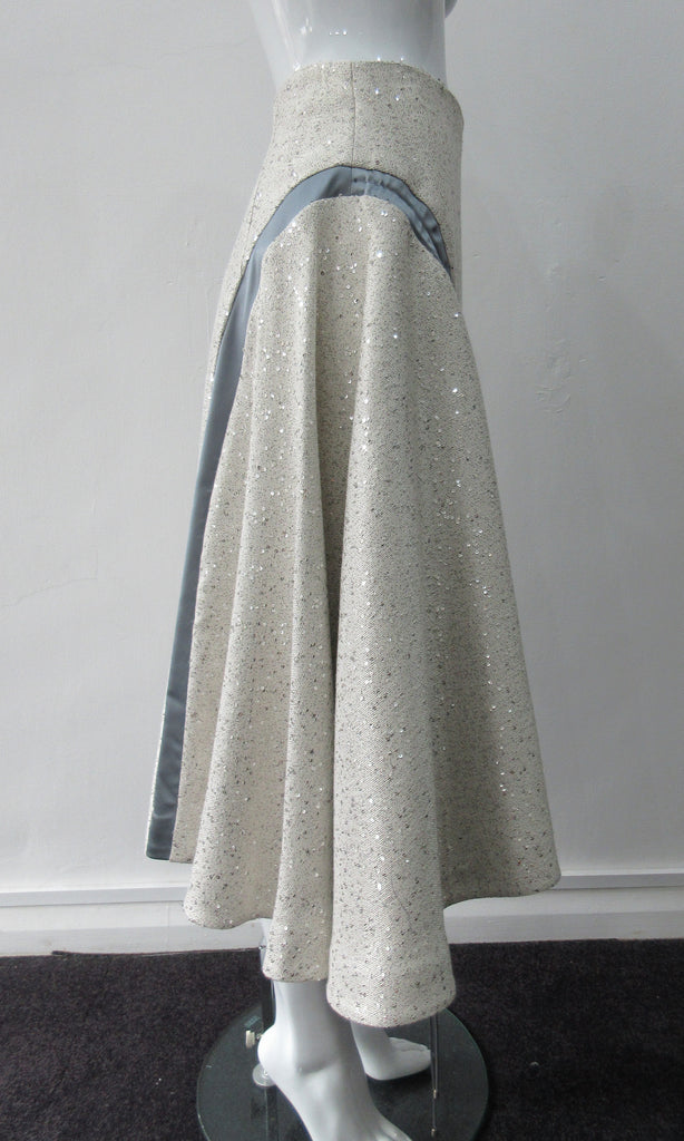 Plain Curve Panel Skirt Assymetrical gathered toggled skrit in grey-white colour. Grey seam panel can be gathered to create raised ruching effect. Featuring textured tweed style with spaced sequins. Large metal side front detaching zipper. CB length 80cm. 600g approximate weight. 36% Polyester, 28% Viscose, 35% Cotton, 5% Lycra. Dry Clean Only. Made in England