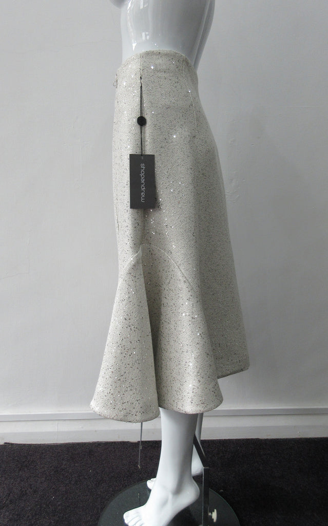 Plain Curve Panel Skirt Assymetrical gathered toggled skrit in grey-white colour. Grey seam panel can be gathered to create raised ruching effect. Featuring textured tweed style with spaced sequins. Large metal side front detaching zipper. CB length 80cm. 600g approximate weight. 36% Polyester, 28% Viscose, 35% Cotton, 5% Lycra. Dry Clean Only. Made in England