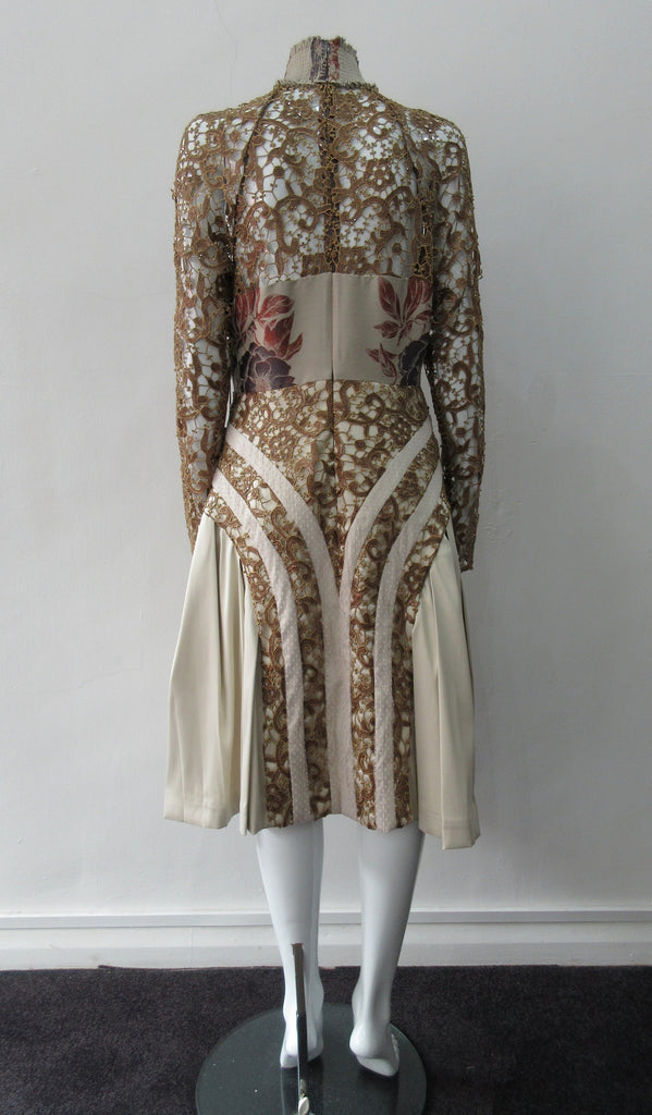 Floral Tri-Point Swing Dress. Intese pleated A-line pleated swing dress in Beige. Contrast sequined and beaded gold lace contrast panels. Subtle floral design on bodice. Full pleats below hip. CB invisible zipper. High ruched collar 6.5cm height. CB length from neck point 105cm. 1kg approximate weight. 100% Polyester, Contrast: 41% Polyester, 26% Acrylic, 26% Wool, 7% Polyamide Lining: 100% Rayon. Dry Clean Only. Made in England