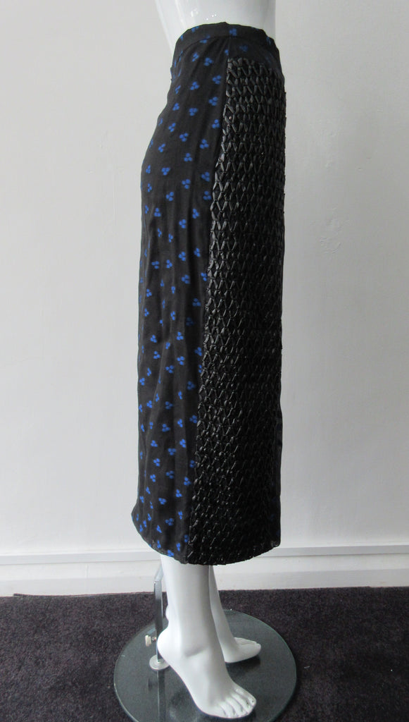 Dark Curve Front Pencil Skirt. Slightly tighter pencil-style fit skirt in sheer black with tri-blue dot design, and black faux leather textured weave design. Can be paired with 180609B Dark Gathered Top. CB length to hem 79cm. 32cm concealed vent bottom of skirt. 400g approximate weight. Fully lined. 90% Polyester, 10% Cotton. Contrast: 100% Polyester. Dry Clean Only. Made in England