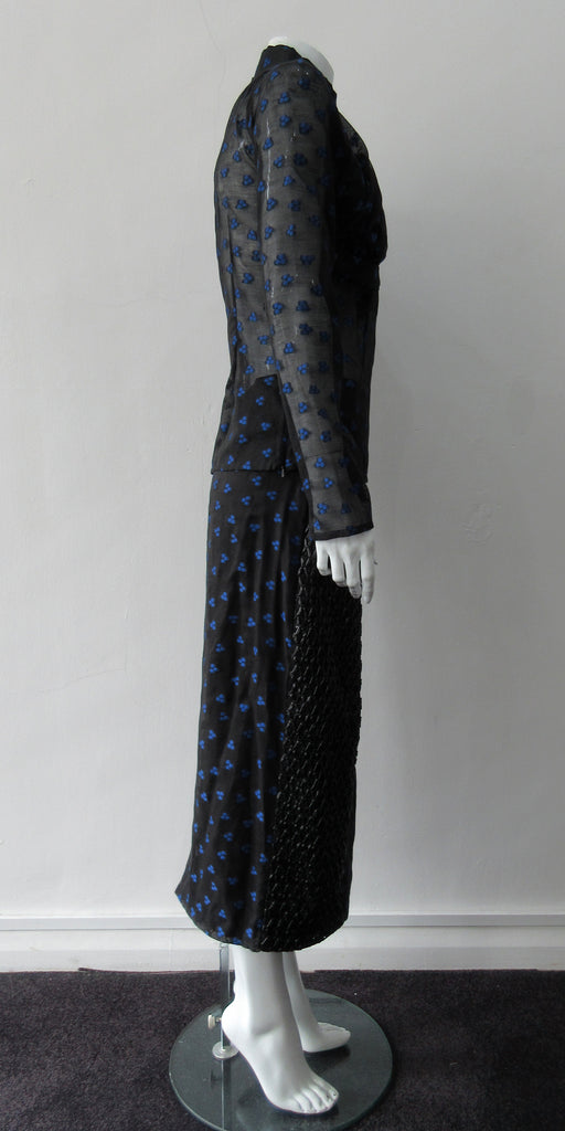 Dark Curve Front Pencil Skirt. Slightly tighter pencil-style fit skirt in sheer black with tri-blue dot design, and black faux leather textured weave design. Can be paired with 180609B Dark Gathered Top. CB length to hem 79cm. 32cm concealed vent bottom of skirt. 400g approximate weight. Fully lined. 90% Polyester, 10% Cotton. Contrast: 100% Polyester. Dry Clean Only. Made in England