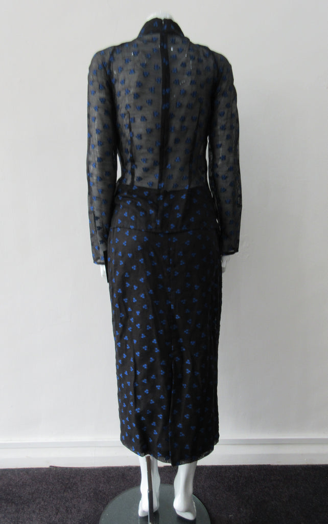 Dark Curve Front Pencil Skirt. Slightly tighter pencil-style fit skirt in sheer black with tri-blue dot design, and black faux leather textured weave design. Can be paired with 180609B Dark Gathered Top. CB length to hem 79cm. 32cm concealed vent bottom of skirt. 400g approximate weight. Fully lined. 90% Polyester, 10% Cotton. Contrast: 100% Polyester. Dry Clean Only. Made in England