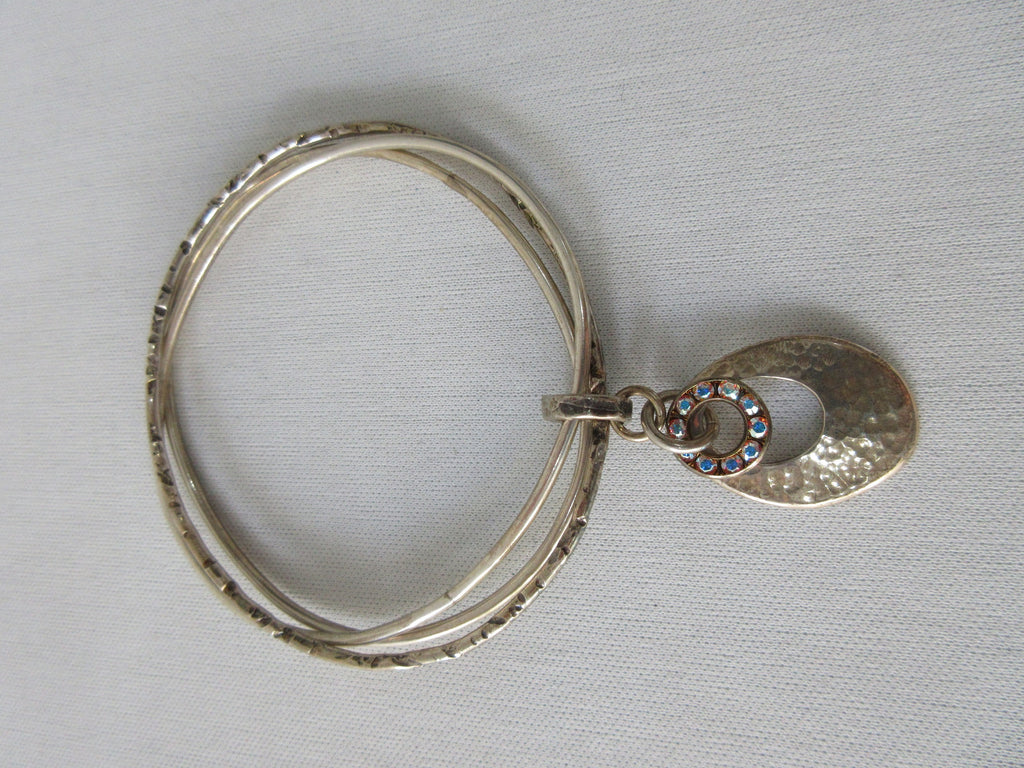 Karyn Chopik Multi 3 Ring Bracelet with Hollow Teardrop and Crystal Ring, 3 Sterling Silver Rings, 1 textured with Brass Ring attachment Size: Medium x1 6.5cm Inside diameter. 35 grams approximate weight. Made in Canada