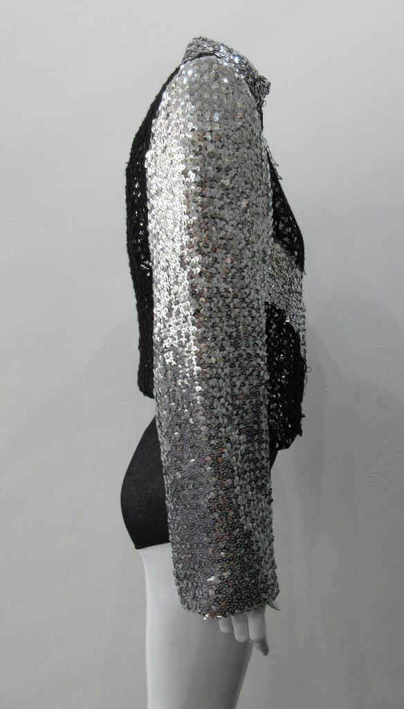 Silver Glitter Jacket with Black Crochet. Full on glittered siver colour sequin jacket with partblack crochet covered for a sporty feel. Crochet detailing unravelling/fraying in areas as done for intentional effect. CF zipper with 8.5cm high collar.  CB length 52cm. Sleeve length from side neck point 76cm. 950g approximate weight. 90% Polyester, 5% Elastine, 5% Metallic Contrast: 100% Cotton. Lining: 100% Polyester. Dry Clean Only. Made in England