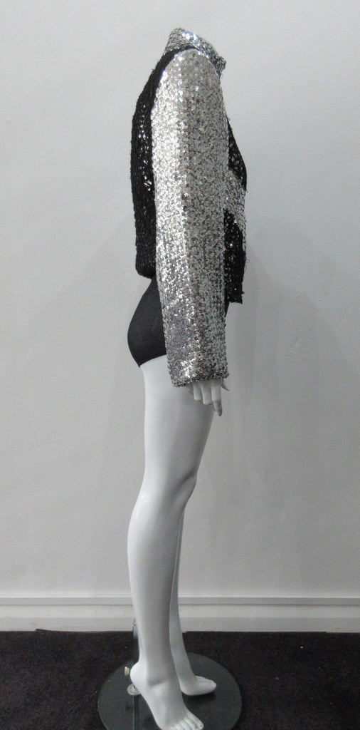 Silver Glitter Jacket with Black Crochet. Full on glittered siver colour sequin jacket with partblack crochet covered for a sporty feel. Crochet detailing unravelling/fraying in areas as done for intentional effect. CF zipper with 8.5cm high collar.  CB length 52cm. Sleeve length from side neck point 76cm. 950g approximate weight. 90% Polyester, 5% Elastine, 5% Metallic Contrast: 100% Cotton. Lining: 100% Polyester. Dry Clean Only. Made in England