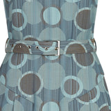 Spot Pleat Dress. Elegant sleevelss dress in multi seagreen circle design in the wovn fabric. Cirular cut away below neck on front of dress with attached collar. Side pleats below hip for ease of movement. Belt and silver buckle. Collar height 3cm. CB length from neck point 97cm. 150g approximate weight. 60% Cotton, 40% Polyester. Dry Clean Only.Made in England
